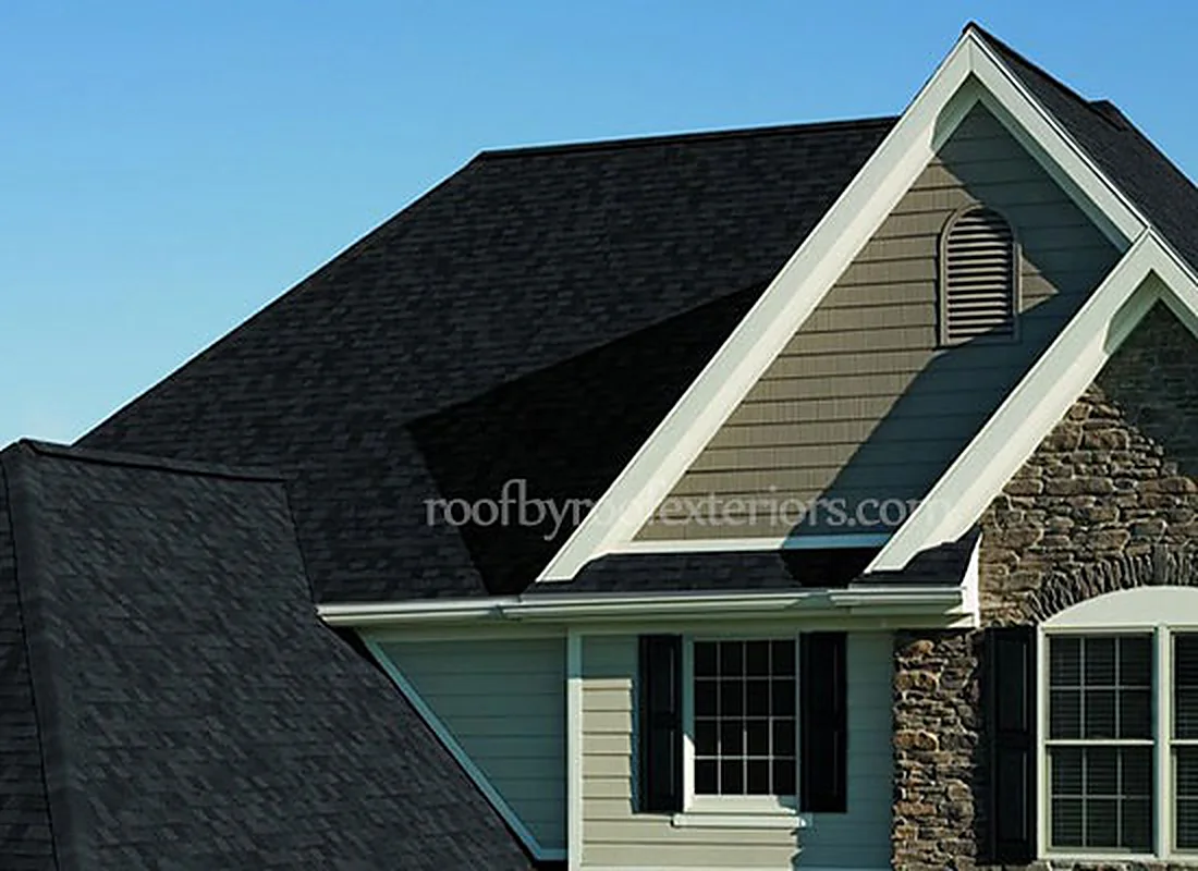 Black shingle gable with white fascia and soffit above a stone wall