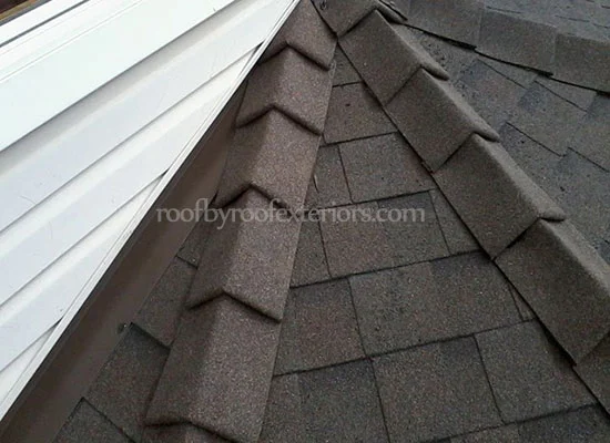 Brown ridge cap shingles meeting white siding